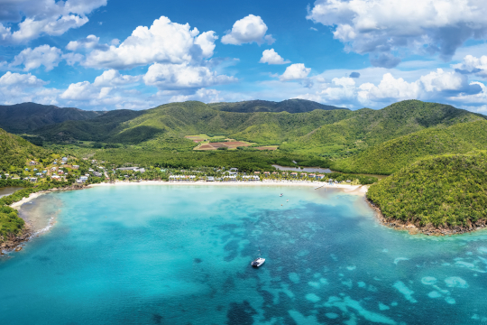 Blick vom Meer aus auf eine grün bewachsene Bucht in der Karibik
